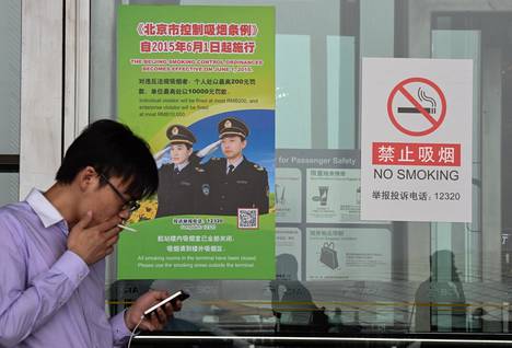 Kiinalainen poltti tupakkaa tupakointikieltokyltin vieressä samana päivänä, kun Pekingissä alettiin tiukasti valvoa tupakointikieltoa kesäkuussa 2015.