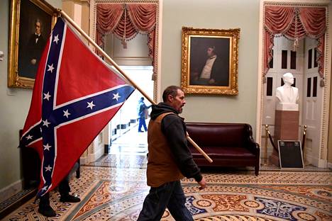 Mies kantaa Yhdysvaltain sisällissodassa orjien omistusta puolustanutta Amerikan konfederaation taistelulippua Capitolissa tammikuussa vuonna 2021.