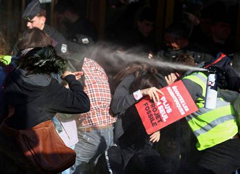 Mielenosoittajat suojautuivat suihkutukselta Total Energies -yhtiön vastaisessa mielenosoituksessa perjantaina. 