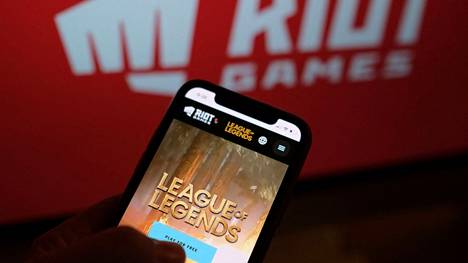 Riot Gamesin suositu League of Legends -peli älypuhelimen näytöllä yhtiön logon näkyessä taustalla.