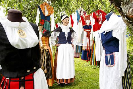 Mari Varonen kotipihallaan pukujen ympäröimänä. Varosella on päällään Keski-Suomen kansallispuku.