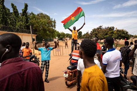 Mies heiluttaa lippua protestoijien parissa perjantaina Burkina Fason pääkaupungissa. Paikalle on sijoitettu sotilaita vallankaappauksen yhteydessä.