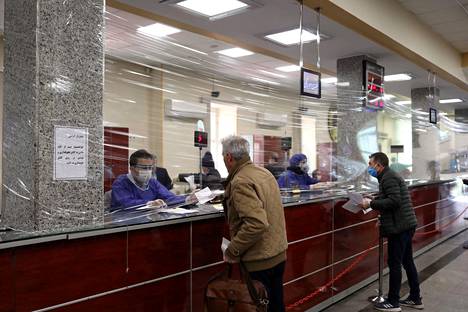 Pankit työntekijät palvelivat asiakkaita muovikelmun takaa pukeutuneina suojavarusteisiin Teheranissa tiistaina.