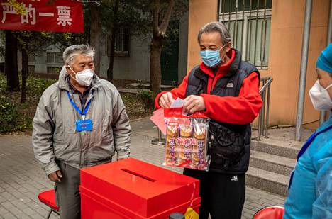 Pekingiläinen äänestäjä on panemassa uurnaan vaaleanpunaista äänestyslippuaan. Lipun edessä hänellä on pussissa päivän leipäostoksia.