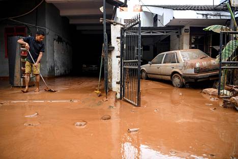 Mies siivosi tulvien jäljiltä kertynyttä savea Bintaron alueella Jakartassa perjantaina.