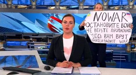 Marina Ovsjannikova heilutti ”Ei sotaa” -julistettaan Vremja-uutislähetyksen ankkurin Jekaterina Andrejevan selän takana. 