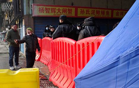 Torikauppias keskusteli vartijoiden kanssa suljetun kalatorin edustalla Wuhanissa sunnuntaina. Toria on epäilty taudin puhkeamisen keskipisteeksi.