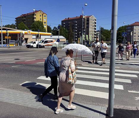 Aurinkovarjolla itseään suojaava jalankulkija ylittää suojatietä Helsingissä 7. kesäkuuta.