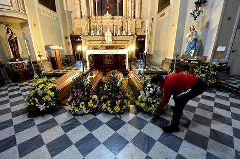 Floristi asettelee seppelettä arkkujen eteen kirkossa Serinan kylässä Pohjois-Italiassa sunnuntaina.
