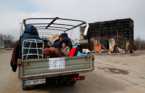 Mariupolin asukkaita pakenemassa auton lavalla pahoin tuhoutuneesta kaupungista torstaina.