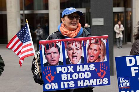 Mielenosoittaja protestoi Fox News -kanavaa vastaan New Yorkissa helmikuun alussa. Mielenosoittajien mukaan Fox oli vastuussa siitä, että Donald Trumpin levittämät valheet vaalivilpistä vuoden 2020 presidentinvaaleissa johtivat väkivaltaan ja ihmisten kuolemiin. Julisteessa on kuvat Foxin tunnetuimmista ankkureista Tucker Carlsonista, Sean Hannitystä ja Laura Ingrahamista.