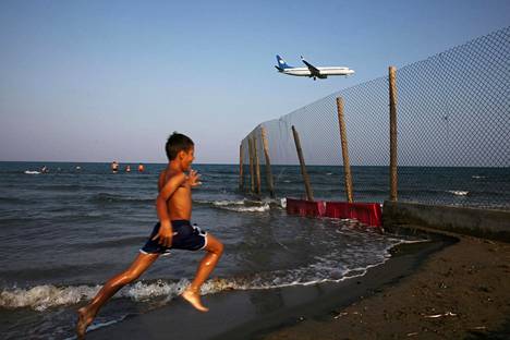 Pikkupoika juoksee rannalla Kyproksella kun matkustajakone lähestyy Larnacan lentokenttää.