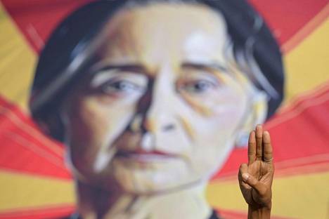Mielenosoittaja näytti Nälkäpeli-kirjasarjasta tunnetuksi tullutta kolmen sormen tervehdystä viime vuoden helmikuussa. Taustalla on kuva syrjäytetystä valtiokanslerista Aung San Suu Kyistä.