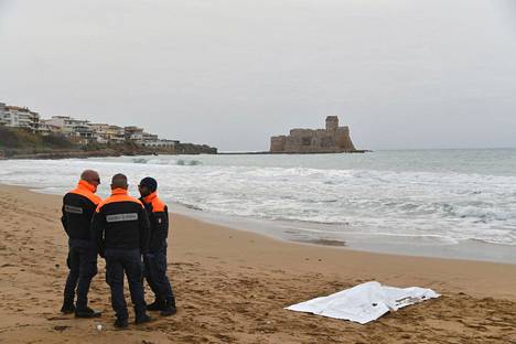 Italian rannikkovartioston jäseniä rannalla Crotonessa maanantaina. Valkoisen peitteen alla makasi haaksirikon uhri.