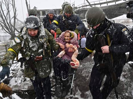 Ukrainalaiset sotilaat auttoivat iäkästä naista ylittämään tuhotun sillan evakuoinnin yhteydessä Irpinin kaupungissa Ukrainassa 8. maaliskuuta.