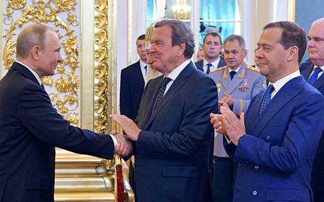 Vuonna 2018 neljättä presidenttikauttaan aloittava Vladimir Putin (vas.) kätteli Gerhard Schröderiä Kremlissä Putinin virkaanastujaisissa. Oikealla tilannetta seuraa Dimitri Medvedev. Taustalla myös nykyinen Venäjän puolustusministeri Sergei Šoigu.