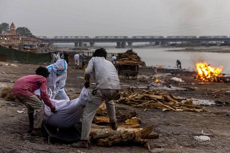 Miehet valmistautuivat polttohautaaman koronaviruksen kuolleen sukulaisensa Ganges-joen rannalla Uttar Pradeshissa viime viikolla.