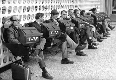 Montrealin lentoasemalla on odottelevien matkustajien käytettävissä televisiovastaanottimia. Ne toimivat kolikoilla puoli tuntia kerrallaan. Katselu näyttää kiinnostavan vain miehiä. Valokuvaajan mukaan naisten aika kuluu lentoaseman naistenhuoneessa.