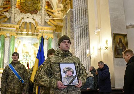 Sotilas piteli Venäjän hyökkäyksessä kuolleen tiedustelu-upseerin Eduard Štrausin kuvaa muistojumalanpalveluksessa Kiovassa maanantaina.