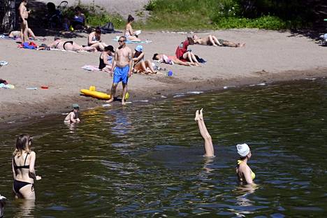 Ihmiset nauttivat auringosta ja uimisesta Marjaniemen uimarannalla Helsingissä juhannusviikonloppuna. Kaupunki ei suosittele uimaan rannalla heikon vedenlaadun takia.