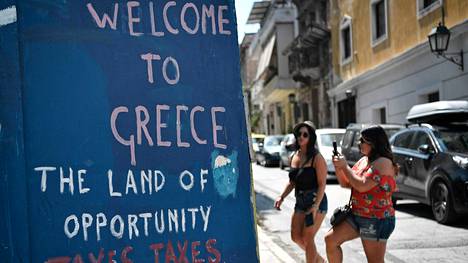 Juliste Ateenassa toivottaa tervetulleksi Kreikkaan ”mahdollisuuksien maahan”. ”Veroja, veroja ja lisää veroja.”