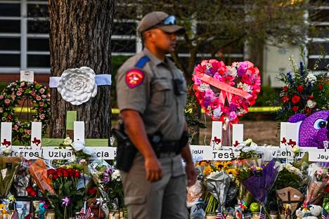 19 lasta ja kaksi aikuista kuoli ampumisessa Robbin peruskoulussa Uvaldessa Texasissa. Viranomainen kuvattuna ampumisen uhrien muistomerkkien lähettyvillä peruskoulun edustalla toukokuun 27. päivänä.