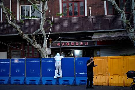 Suojavarusteisiin pukeutunut ihminen katsoo aidan yli Shanghaissa maanantaina. Aidoilla on rajattu sulkutoimien kohteena olevat alueet.