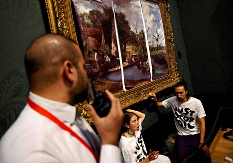 Just Stop Oil -aktivistit vastustavat öljyyn liittyviä energiahankkeita. He kiinnittivät oman kuvansa maalaismaisemamaalauksen päälle Lontoossa.