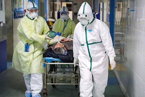 Suoja-asuihin pukeutuneet sairaalatyöntekijät kuljettivat potilasta eristysosastolla Caidianni alueella Kiinassa 6. helmikuuta.