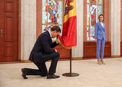 Uusi pääministeri Dorin Recean polvistuu Moldovan lipun edessä. Taustalla presidentti Maia Sandu.