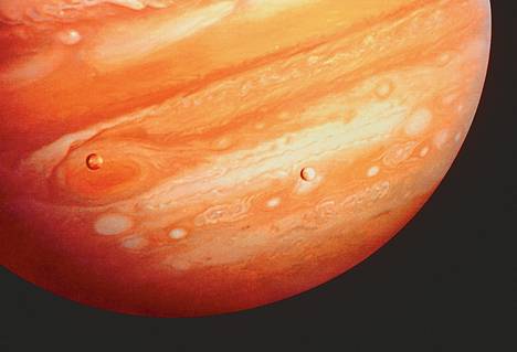 Punainen pilkku näkyy planeetan kaasukehässä vasemmalla. Pilkun päällä näkyy kuu Io. Valokuvan otti luotain Voyager 1 vuonna 1979.
