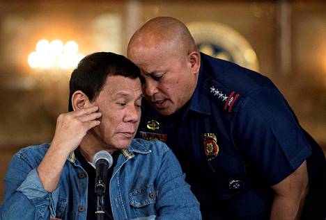 Filippinien poliisivoimien komentaja Ronald Dela Rosa kumartui kuiskaamaan presidentti Rodrigo Dutertelle kesken lehdistötilaisuuden. Kuva on talvelta 2017. 