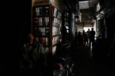 Mies istui kauppansa edessä sähkökatkon aikana Karachissa maanantaina.