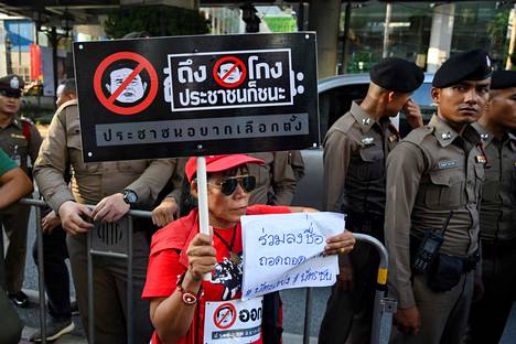 Sotilasjunttaa ja vaalivilppiä vastustanut mielenosoittaja esitteli kylttiään turvallisuusjoukkojen edessä Bangkokissa sunnuntaina.