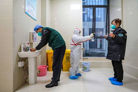 Täysissä suojavarusteissa oleva työntekijä desinfioi ambulanssihenkilökuntaa Kiinan Wuhanissa sunnuntaina.