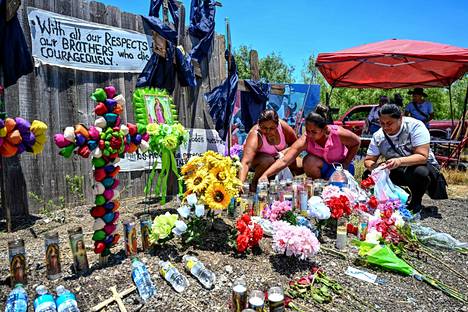 Ihmiset tuovat kynttilöitä, kukkia ja vesipulloja kuorma-auton perävaunuun kuolleiden siirtolaisten muistomerkille San Antonion kaupungin liepeillä Texasissa. 