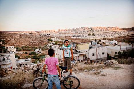 9-vuotias Amin ja 7-vuotias Hakim kuvattuna vuonna 2014 Wadi Fukin kylässä. Taustalla Israelin uusi siirtokunta Palestiinan miehitetyllä Länsirannalla. 