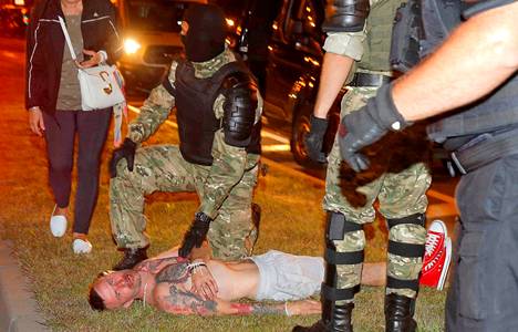 Poliisit pitivät maassa makaavaa miestä paikallaan Minskissä sunnuntai-iltana.