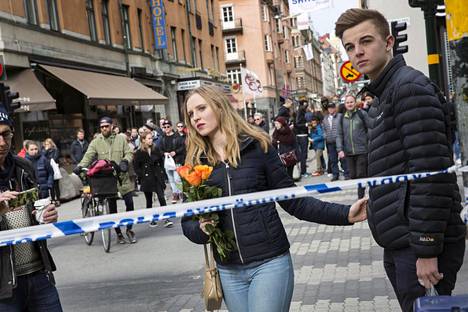 Ihmiset toivat turmapaikalle kukkia terrori-iskun uhrien muistoksi Tukholman Drottningsgatanilla lauantaina.