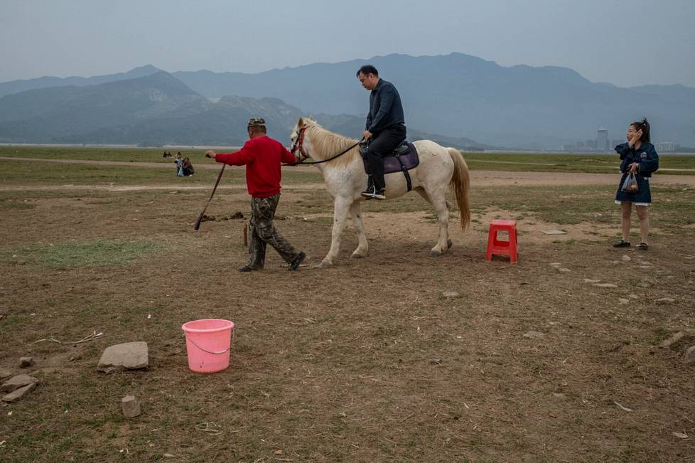 Turistit ratsastivat harvakseltaan valkoisella hevosella kuivuneella järvenpohjalla. Selässä ollut mies valitti, kun hevonen ei suostunut ravaamaan.