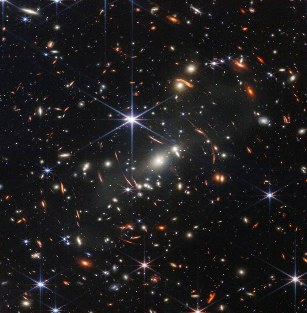 Avaruusteleskooppi James Webbin ensimmäinen julkaistu värikuva. Kuvan punertavat  kaaret ja pallukat ovat säteilyä galakseista hyvin varhaisessa universumissa. Webbin tarkka kamera NIRCam toi nämä galaksit näkyviin ensi kertaa. Niissä on  rakenteita, joita ihmisen silmä ei ole koskaan aiemmin nähnyt.