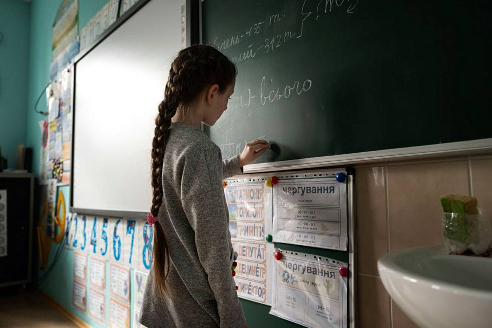 A girl named Lisa writes on a blackboard at a school in the city of Krasnogorivka.  Some students have been sent home, some are studying at dusk because the school does not dare to keep the lights on.