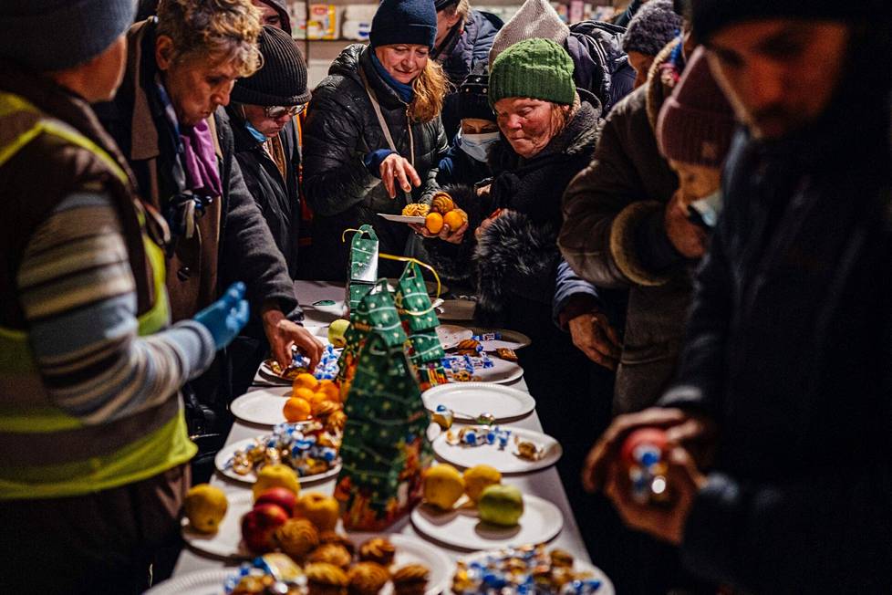 Paikalliset asukkaat kokoontuvat joulupöydän ääreen tarjoilemaan pieniä kakkuja ja hedelmiä humanitaarisessa avustuskeskuksessa Bahmutissa, 6. tammikuuta.