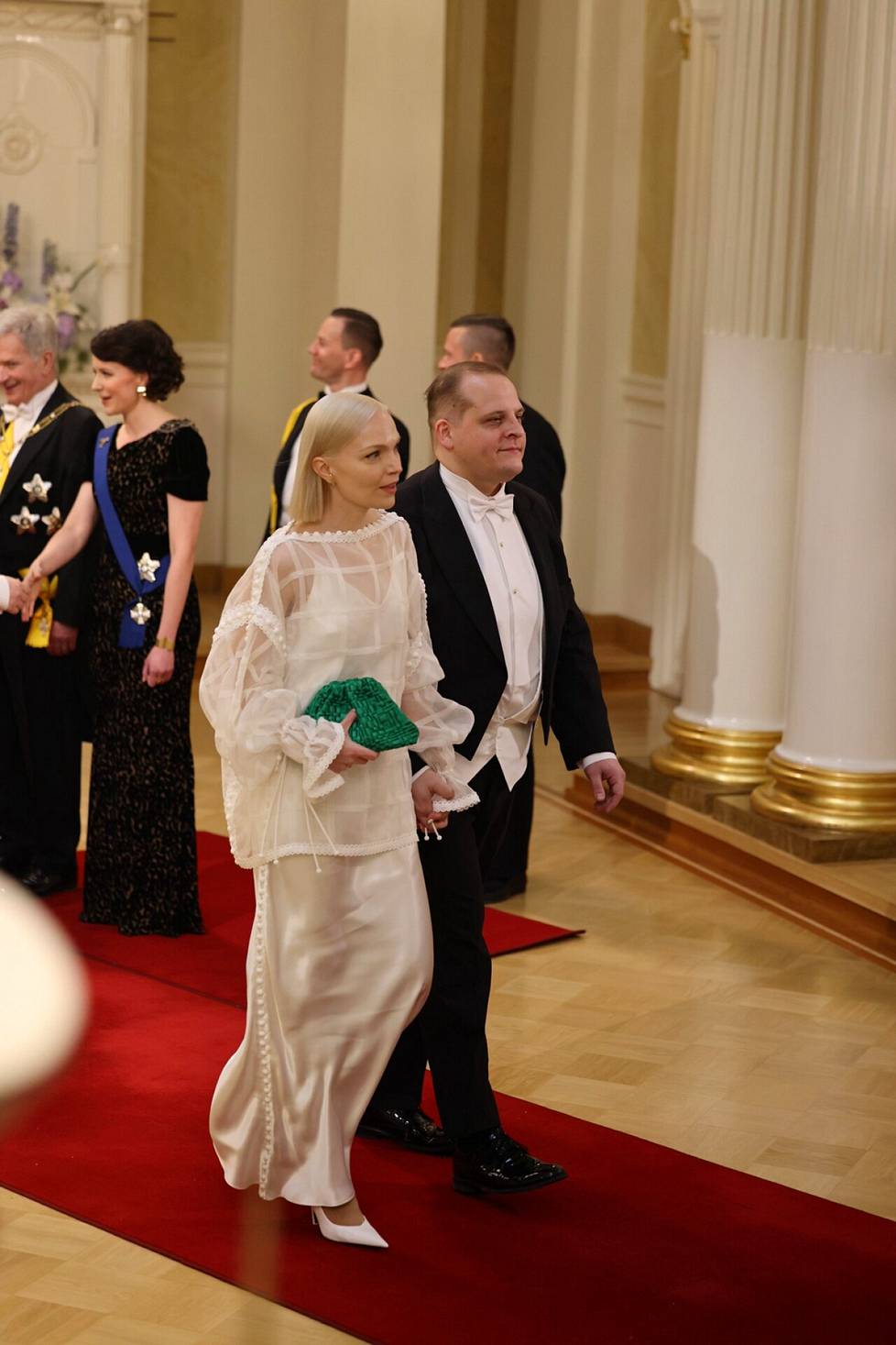 MP Minja Koskela's (left) white suit is two-piece.  Silk organza and viscose satin have been used as materials.  Next to her husband, the director Oskari Sipola.