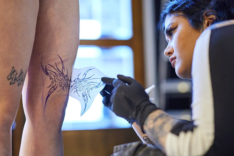 Tattoo artist Elisa Kiljunen prints an image printed on stencil paper onto Iida Rantanen's skin.  The purpose of the picture is to help with tattooing.