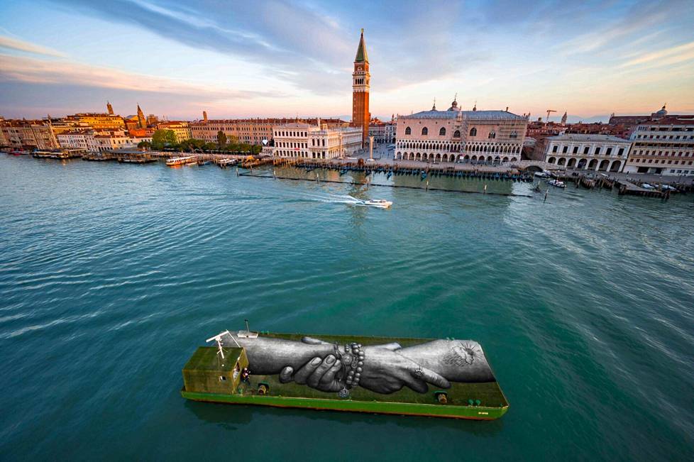 Ilmakuva Venetsiasta huhtikuun 19. päivänä, Venetsian biennaalin avajaisviikolla. Etualalla ranskalais-sveitsiläisen Guillaume Legrosin eli Saypen kelluva, maatuva ympäristötaideteos. Beyond Walls -projektiin kuuluva teos liikuskelee Venetsian vesillä biennaalin aikana.