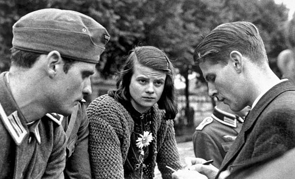 München 22.7.1942. Sophie Scholl saattamassa veljeään Hansia (vas.) ja paria muuta tuttua nuorta miestä heidän lähtiessään itärintamalle suorittamaan lyhyttä asevelvollisuusaikaa lääkintämiehinä. Oikealla on Christoph Probst. He kaikki olivat salaisen Valkoinen ruusu -vastarintaryhmän jäseniä, ja tasan seitsemän kuukautta myöhemmin heidät teloitettiin giljotiinilla. – Englundin kirjan kuvitusta.