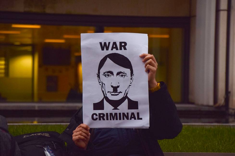 Mielenosoittaja Lontoossa 15. maaliskuuta piti esillä sotarikollinen-tekstiä ja kuvaa, joka on yhdistelmä Vladimir Putinista ja Adolf Hitlerin kampauksesta ja viiksistä.