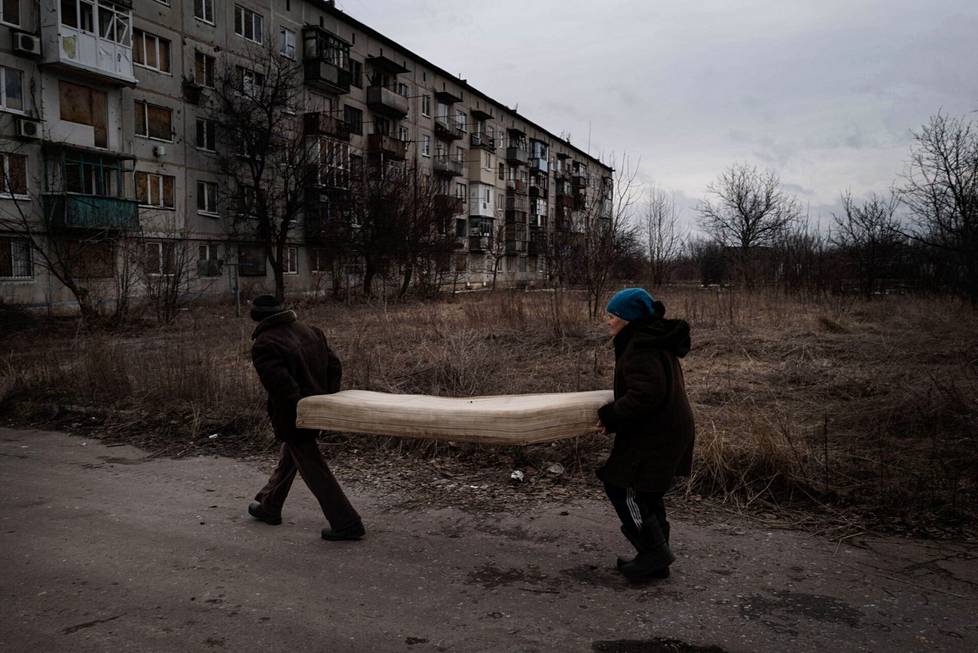 A woman named Alla and her husband carry a mattress they find in the trash on the outskirts of Krasnohorivka, where few live anymore.