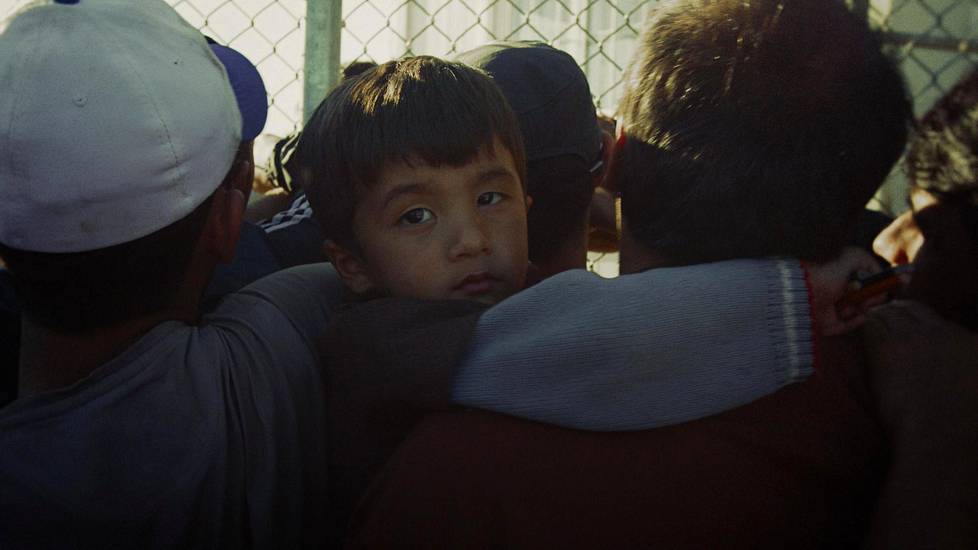 Poika odottaa jonotusnumeroa Lesboksen pakolaisleirillä isänsä sylissä. Värikynät on.
